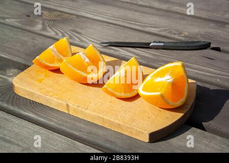 appetitosi pezzi tagliati di frutta d'arancia su tagliere su tavola marrone di legno sulle luci del sole con coltello. mangiare sano, frutta, estate Foto Stock