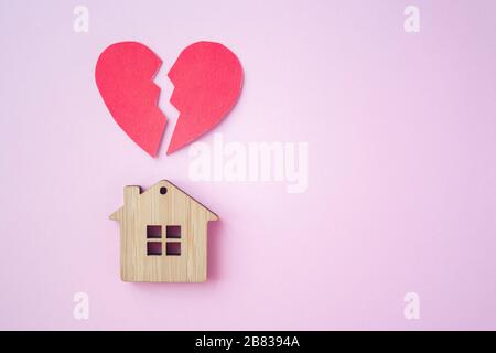 Divorzio, divisione della proprietà, povertà e nessun concetto di denaro. Casa di legno con cuore rotto su sfondo rosa brillante. Ipoteca, affitto, realtor Foto Stock