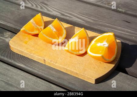 appetitosi pezzi tagliati di frutta d'arancia sul tagliere su un tavolo marrone di legno sulle luci del sole. mangiare sano, frutta, estate Foto Stock