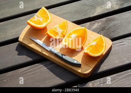 appetitosi pezzi tagliati di frutta d'arancia sul tagliere su tavola marrone di legno sulle luci del sole con coltello. mangiare sano, frutta, lato estivo Foto Stock