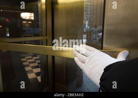 Un residente di New York spinge una porta girevole con una mano con i guanti come precauzione contro i germi durante la Pandemia COVID-19, USA Foto Stock