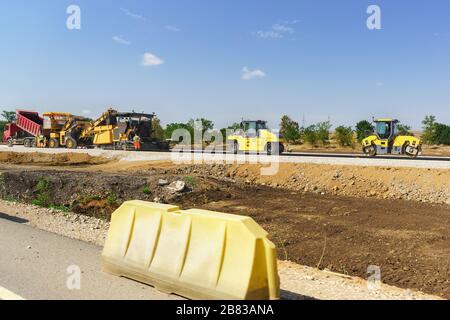 Costruzione di una nuova strada Tavrida in Crimea. Rulli gialli e finitrici. Giorno estivo soleggiato Foto Stock