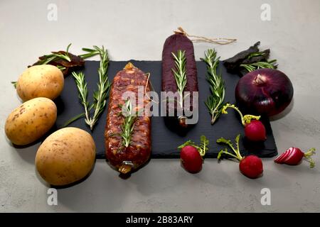 Affumicato affumicato con rosmarino e verdure su un ardesia nero su sfondo grigio, vista frontale ad angolo. Foto Stock