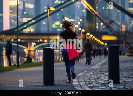 19 marzo 2020, Hessen, Francoforte sul meno: Una donna sta facendo jogging sulla riva del fiume meno. Nonostante la pandemia di Corona, la gente sta passeggiando lungo le rive del Main e nel parco portuale parzialmente chiuso. Foto: Andreas Arnold/dpa Foto Stock