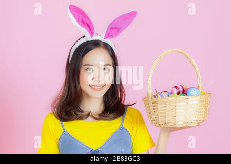 Ritratto di una giovane donna felice che indossa orecchie di coniglio di Pasqua si prepara a celebrare la Pasqua su uno sfondo rosa. Foto Stock