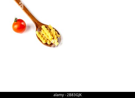 Pasta italiana secca cruda in cucchiaio di legno con pomodoro su fondo bianco. Concetto di cibo e bevande. Vista dall'alto. Spazio di copia Foto Stock