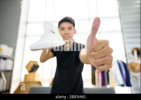 Social media influencer che rivede la moda scarpe. Sorridente giovane uomo che vlogging circa la scarpa sportiva degli uomini e filmarsi a casa su una videocamera. Foto Stock