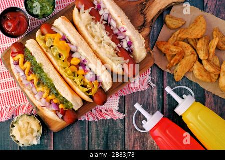 Hot dog con condimenti assortiti e zeppe di patate, scena aerea su uno sfondo rustico in legno Foto Stock