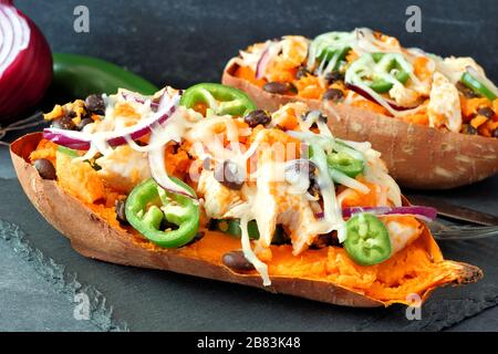 Patate dolci al forno farcite con pollo, verdure e formaggio, primo piano su sfondo scuro Foto Stock