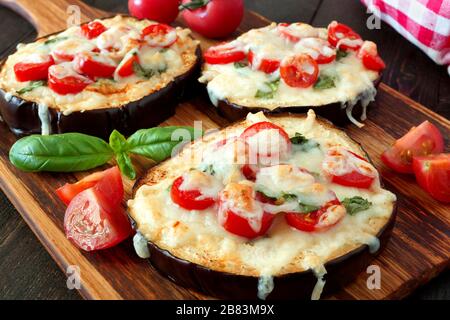 Mini pizze di melanzane sane con mozzarella fusa, pomodori e basilico, primo piano su un tabellone Foto Stock