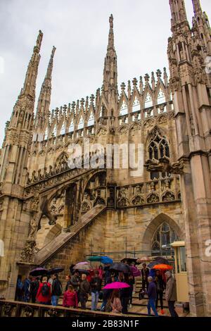 Turisti che visitano e godono la vista circondata dalle guglie e statue al tetto della Cattedrale di Milano in primavera piovosa giorno, Italia, maggio 2017 Foto Stock