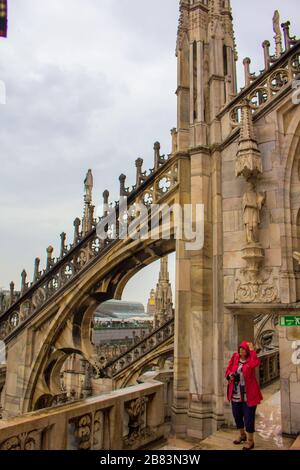 Donna turistica in rosso visita e godendo la vista e le guglie e statue al tetto della Cattedrale di Milano in primavera piovosa giorno, Italia, maggio 2017 Foto Stock