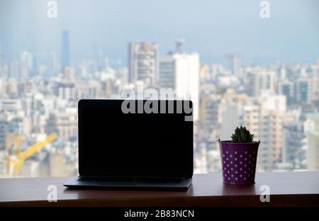 Computer portatile e impianto di cactus in una pentola al tavolo o scrivania al 21 ° piano con una splendida vista della città. Foto scattata a Beirut, Libano Foto Stock