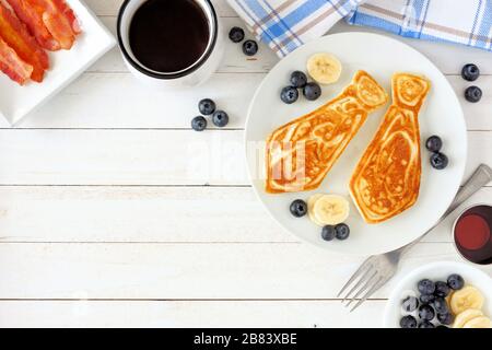 Frittelle a forma di cravatta con mirtilli e banane. Concetto di colazione per il giorno dei padri. Bordo dell'angolo della vista superiore su sfondo di legno bianco. Foto Stock