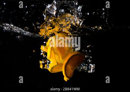 Arance a fette che cadono nell'acqua con cubetti di ghiaccio. Concetto di mangiare sano Foto Stock