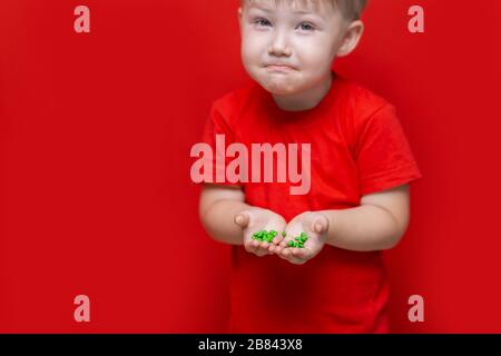 piccolo ragazzo triste tenere un sacco di pillole in mano. t-shirt rossa, sfondo rosso pericoloso concetto, compresse e bambino Foto Stock