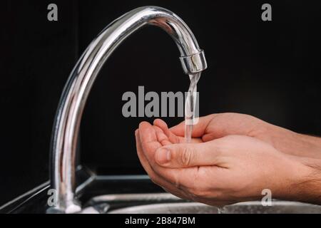 mani di un uomo che beve dell'acqua che scorre attraverso le sue dita rinfrescando e lavando mentre lui in cucina. L'acqua riempie il palmo della mano. Igiene Foto Stock