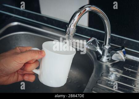 Moderno rubinetto e lavandino in cucina. Uomo che versa una bevanda fresca a tazza. Riempire il vetro bianco con acqua di rubinetto. Foto Stock