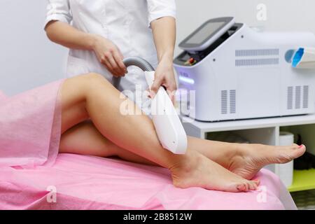 Primo piano di una cosmetologa femminile in un cappotto medico che rende una giovane donna una procedura laser rimozione dei capelli per la gamba. Cosmetologia, ionizzazione, diamante pro Foto Stock