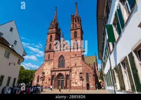 Un gruppo di turisti aspetta di fronte al Basilea Minster in una bella giornata di sole con cielo blu. Con le sue pareti di arenaria rossa, le piastrelle colorate del tetto... Foto Stock