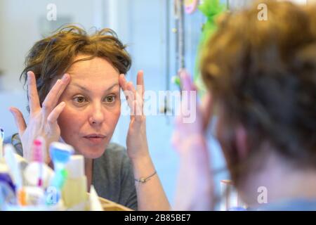 Donna ispanica che controlla il suo viso in uno specchio durante le sue abluzioni mattutine con una vista al suo riflesso nello specchio Foto Stock