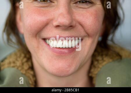 Donna felice che dà un sorriso toothy del fascio in un primo piano con fuoco selettivo sulla sua bocca Foto Stock