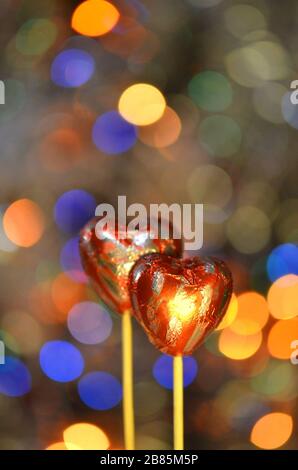 Caramelle al cioccolato per San Valentino. Cioccolato a forma di cuore rosso su bastone lolly. Cuore di cioccolato in lamina rossa su un bastone su uno sfondo sfocato bokeh Foto Stock