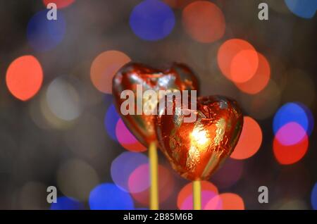 Caramelle al cioccolato per San Valentino. Cioccolato a forma di cuore rosso su bastone lolly. Cuore di cioccolato in lamina rossa su un bastone su uno sfondo sfocato bokeh Foto Stock