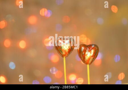 Caramelle al cioccolato per San Valentino. Cioccolato a forma di cuore rosso su bastone lolly. Cuore di cioccolato in lamina rossa su un bastone su uno sfondo sfocato bokeh Foto Stock