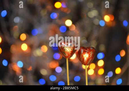 Caramelle al cioccolato per San Valentino. Cioccolato a forma di cuore rosso su bastone lolly. Cuore di cioccolato in lamina rossa su un bastone su uno sfondo sfocato bokeh Foto Stock