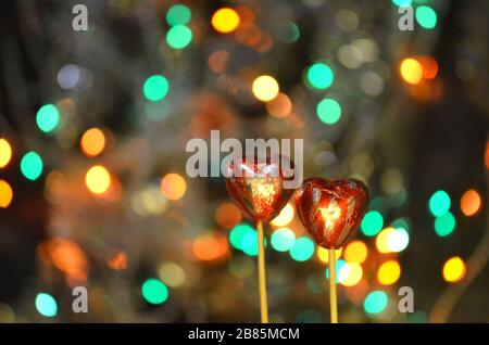 Caramelle al cioccolato per San Valentino. Cioccolato a forma di cuore rosso su bastone lolly. Cuore di cioccolato in lamina rossa su un bastone su uno sfondo sfocato bokeh Foto Stock