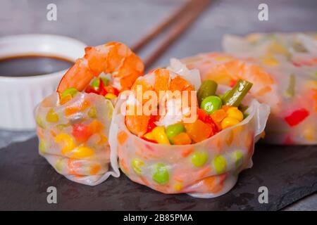 Involtini primavera con verdure e gamberetti in una carta di riso. Vicino al bagno di soia e alle bacchette. Foto Stock