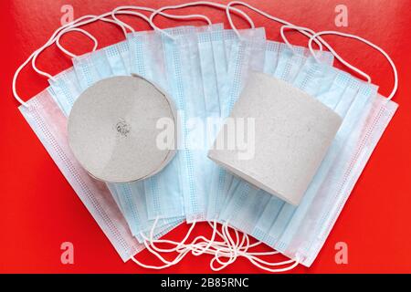 Vista dall'alto dei rotoli di carta igienica sullo sfondo delle maschere antivirali e sullo sfondo di colore rosso. Assicurazione mondiale pandemica, coronavirus, malattie aeree Foto Stock