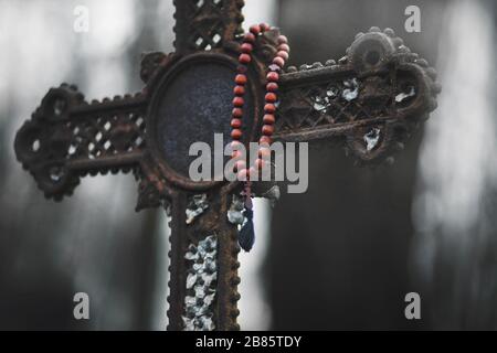 Al crepuscolo, un rosario di legno rosso è appeso su una vecchia croce arrugginita. Foto Stock