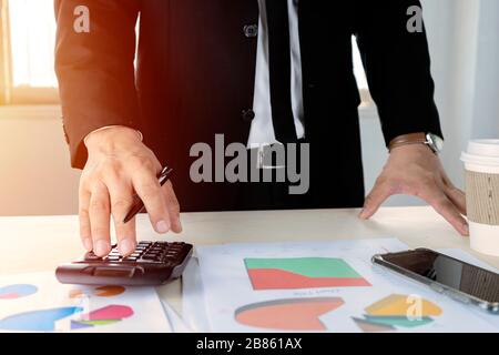 Gli uomini d'affari calcolano con calcolatrici per calcolare costi e profitti. Una buona pianificazione del marketing deve essere prudente. Con analisi da grafico statist Foto Stock