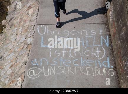 Friburgo, Germania. 20 Marzo 2020. Un jogger corre lungo il Dreisam. Con il gesso è dipinta su: 'A proposito, sorridendo è (non) contagioso @our Freiburg'. A causa della pandemia di Corona, la città di Friburgo ha emesso un coprifuoco per gruppi più grandi. Dal 21 marzo al 3 aprile si applicherà un cosiddetto divieto di accesso ai luoghi pubblici. Credit: Patrick Seeger/dpa/Alamy Live News Foto Stock