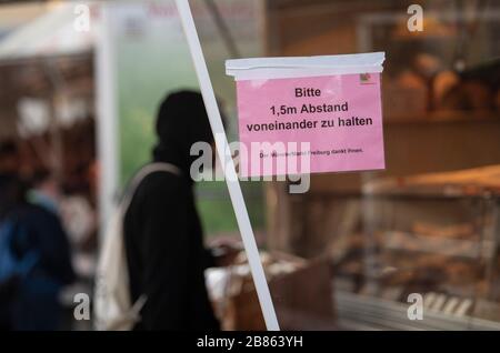 Friburgo, Germania. 20 Marzo 2020. Un uomo negozi al mercato Munster. Al supporto è apposta un'insegna con l'iscrizione 'si prega di mantenere una distanza di 1,5 m l'uno dall'altro'. A causa della pandemia di Corona, la città di Friburgo ha emesso un coprifuoco per gruppi più grandi. Dal 21 marzo al 3 aprile si applicherà un cosiddetto divieto di accesso ai luoghi pubblici. Credit: Patrick Seeger/dpa/Alamy Live News Foto Stock