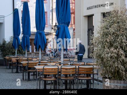 Friburgo, Germania. 20 Marzo 2020. Un uomo cammina davanti ai tavoli vuoti di una caffetteria di Augustinerplatz. A causa della pandemia di Corona, la città di Friburgo ha emesso un coprifuoco per gruppi più grandi. Dal 21 marzo al 3 aprile si applicherà un cosiddetto divieto di accesso ai luoghi pubblici. Credit: Patrick Seeger/dpa/Alamy Live News Foto Stock