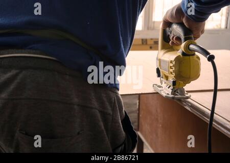 Primo piano di un falegname utilizzando una sega elettrica per tagliare un grande asse di legno. Foto Stock