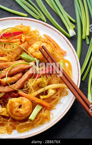 Singapore Mei Fun in bianco piatto su sfondo ardesia scuro. Singapore Noodles è un piatto di cucina cinese con tagliatelle di riso, gamberi, maiale char siu, carota, Foto Stock