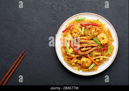 Singapore Mei Fun in bianco piatto su sfondo ardesia scuro. Singapore Noodles è un piatto di cucina cinese con tagliatelle di riso, gamberi, maiale char siu, carota, Foto Stock