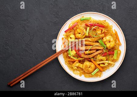 Singapore Mei Fun in bianco piatto su sfondo ardesia scuro. Singapore Noodles è un piatto di cucina cinese con tagliatelle di riso, gamberi, maiale char siu, carota, Foto Stock