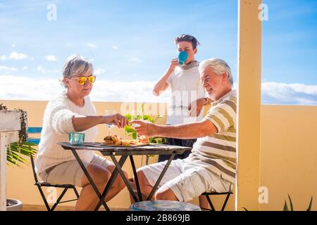 Nonni adulta e matura adolescente nipote gustare all'aperto in terrazza qualche tempo libero con cibo e bevande. oceano e vista sulla città, vacanze giornata di sole Foto Stock