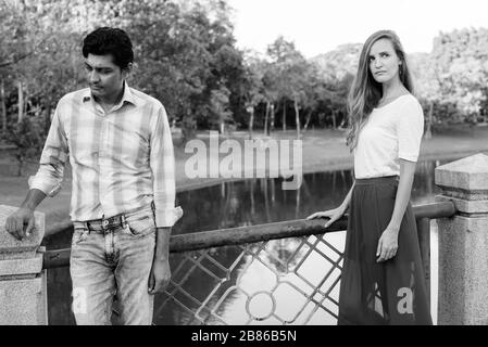 Coppia multietnica che pensa e guarda lontano l'uno dall'altro sul ponte del parco Foto Stock