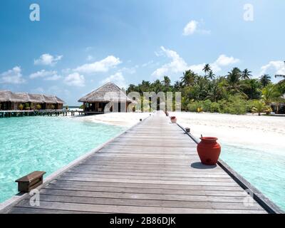 Isola tropicale con palme e Molo di legno nell'Oceano Indiano sulle Maldive. Giorno di sole. Spiaggia tropicale con bungalow sull'acqua e sabbia bianca sulle Maldive Foto Stock