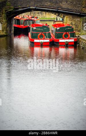 Barche strette dipinte di rosso e bianco sotto un ponte di canale sul canale di Leeds e Liverpool a Skipton , North Yorkshire Foto Stock