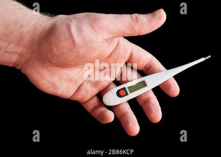 Termometro elettronico in una mano maschile forte su sfondo nero. Fermata Coronavirus. 2019 romanzo Coronavirus (2019-nCoV). Contenuto medico Foto Stock