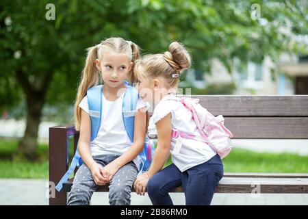 Due bambini piccoli pettegolezzi su una panchina. Il concetto è di ritorno a scuola, famiglia, amicizia e infanzia. Foto Stock