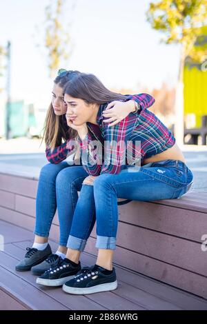 Giovane donna conforta una triste amica femminile nel parco Foto Stock