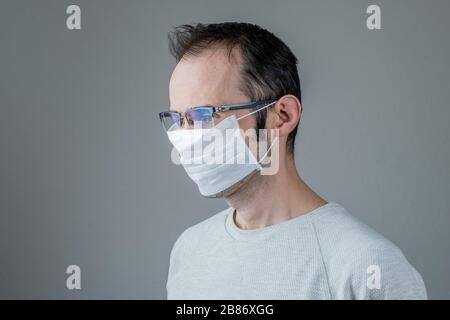 Uomo adulto che indossa una maschera igienica per prevenire le infezioni, malattie respiratorie dell'aria come l'influenza, 2019-nCoV su sfondo grigio. Concetto di assistenza sanitaria. Foto Stock